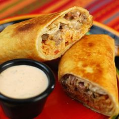 two burritos sitting on top of a red plate next to a small bowl of ranch dressing