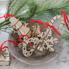 three wooden christmas ornaments on a plate next to a pine branch with red and white ribbon