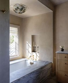 a bath tub sitting next to a window in a bathroom under a chandelier