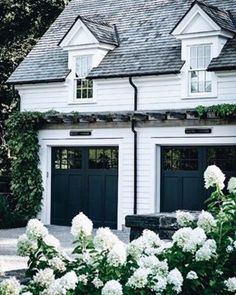 a white house with two black garage doors and some flowers in front of the door