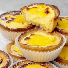 there are many small yellow desserts in the white paper cupcake tins on top of each other