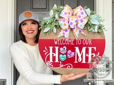 a woman holding up a welcome to our home sign with flowers and hearts on it