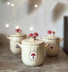 three ceramic pots with red mushrooms on them sitting on a table next to string lights