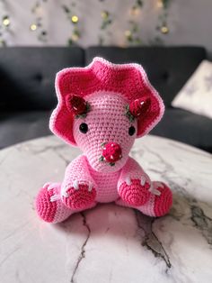 a pink crocheted elephant sitting on top of a white marble table next to a black couch