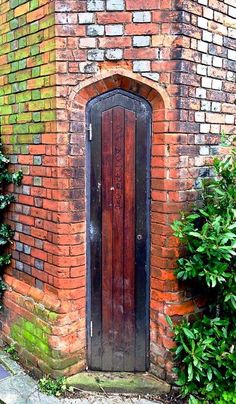 an old red brick building with a wooden door and window in the center surrounded by greenery