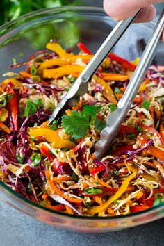 someone is cutting into a colorful salad with tongs