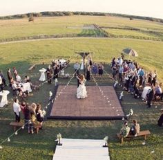 a large group of people standing on top of a lush green field next to a wooden floor