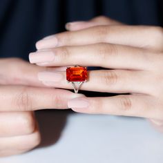 a woman's hand holding a ring with an orange stone on it and her fingers