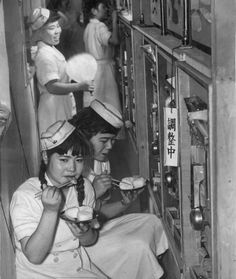 an old black and white photo of women in uniforms eating food from bowls on shelves