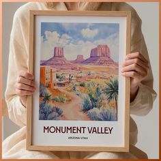 a woman holding up a framed poster with monument valley in the background