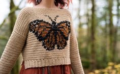 a woman wearing a sweater with a butterfly on it in the middle of a forest