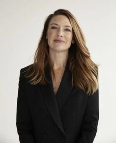 a woman with long hair wearing a black suit and standing in front of a white wall