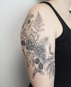 a woman wearing a black tank top with pine cones and berries on her arm,