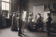 an old black and white photo of people in a room with paintings on easels