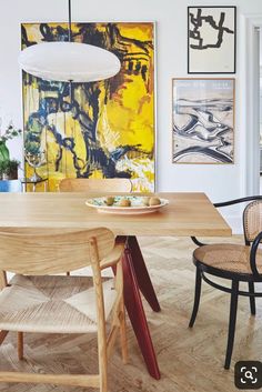 a dining room table with chairs and artwork on the wall