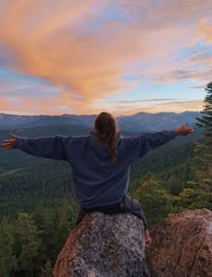 a person sitting on top of a large rock with their arms outstretched in the air