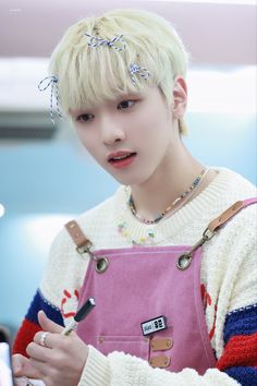 a young man with blonde hair wearing overalls and holding a cell phone