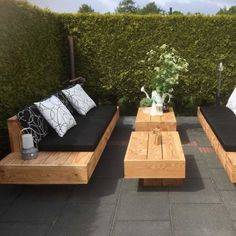 an outdoor seating area with black cushions and white pillows on the couches, in front of a green hedge