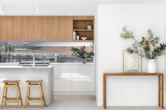 two stools sit in front of a kitchen island with an open window and plants on the counter