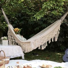 a hammock hanging from a tree near a table with plates and cups on it