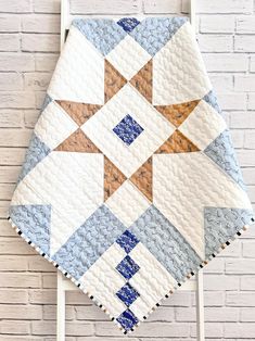 a white chair with a blue and brown quilt on it's back next to a brick wall