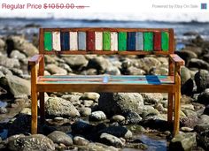 a wooden bench sitting on top of a rocky beach next to the ocean with colorful stripes painted on it