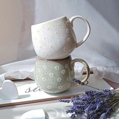 two mugs sitting on top of each other next to some lavender sprigs