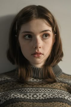 a young woman with brown hair and blue eyes wearing a sweater looking at the camera