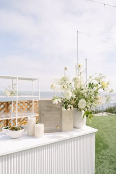 a table with flowers and candles on it in front of an ocean side fenced area