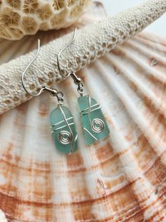 sea glass and silver wire earrings sitting on top of a seashell