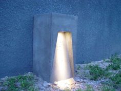 an outdoor light shines brightly on the ground next to a concrete structure with grass growing around it