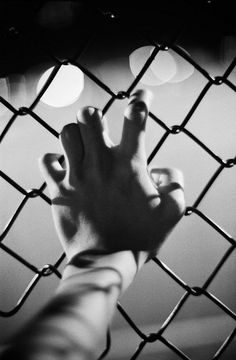 a hand reaching up through a chain link fence