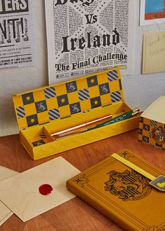 an open yellow box sitting on top of a wooden table next to papers and pencils