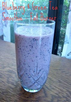 a glass filled with purple liquid sitting on top of a wooden table next to a window