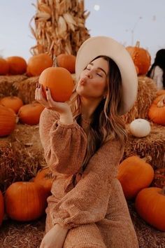 a woman sitting on hay with pumpkins in front of her and looking up at the sky