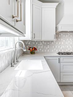 a kitchen with white cabinets and marble counter tops