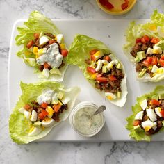 four lettuce cups filled with meat and vegetables on a white platter next to a jar of ranch dressing