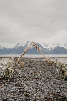 an outdoor ceremony set up with chairs and flowers in front of the mountain range on a cloudy day