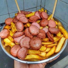 a person holding a metal bowl filled with meat and french fries on skewers