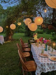 an outdoor dining area with paper lanterns strung from the trees and tables set for dinner