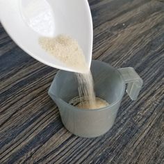 a person pouring sugar into a measuring cup on a wooden table with wood grain in it