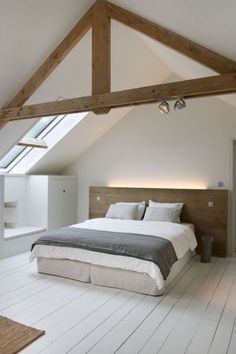 a bed sitting under a window in a bedroom next to a white wall and wooden beams