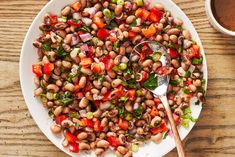 a white plate topped with beans and veggies next to a cup of coffee