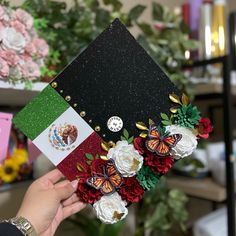 a person holding up a graduation cap with flowers and butterflies on the front, decorated with flags