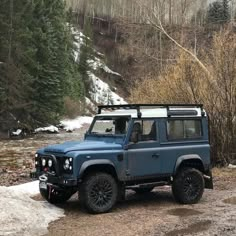 a blue jeep is parked on the side of a road near some trees and snow