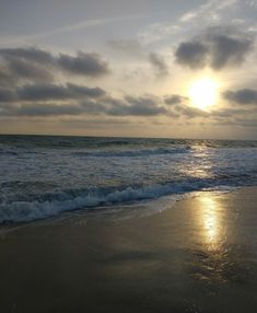 the sun is setting over the ocean with waves lapping in front of it and some clouds