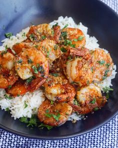 a black plate topped with rice and shrimp on top of a blue checkered table cloth