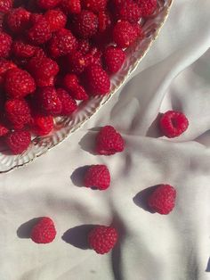 raspberries in a glass bowl on a white tablecloth with the sun shining