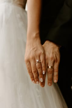 the bride and groom are holding hands with their wedding rings on their fingers as they stand close to each other