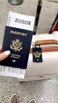 a person holding up a passport in front of an airport baggage claim case and luggage